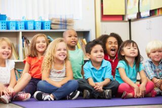 photo - Elementary Students Sitting on Rug in Classroom Listening to Teacher