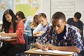 Male Student In Classroom Writing In Notebook