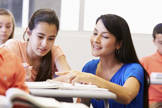 Teacher Helping Female High School Student In Classroom