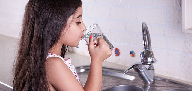 Little girl drinking water from kitchen faucet