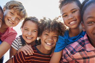 Six pre-teen friends piggybacking in a park, close up portrait