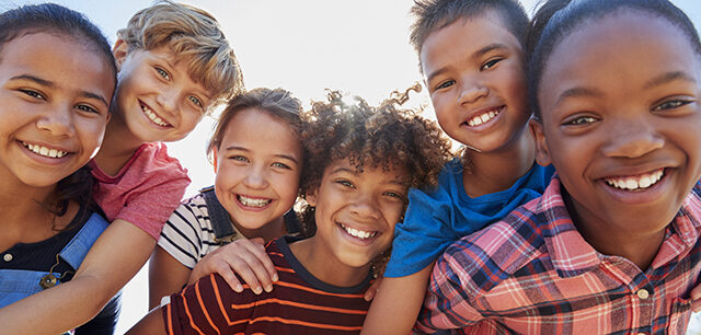 Six pre-teen friends piggybacking in a park, close up portrait