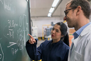 Engineering Student Talking To Her Teacher Trying To Solve A Problem On The Board