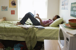 photo - Young Woman Studying on Bed in Dormitory