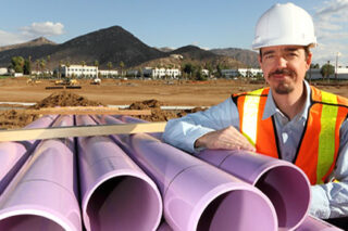 photo - Utility Worker Leans on Stacked Purple Pipe