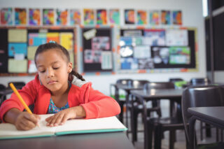 photo - Girl Writing While Sitting at Desk in Classroom