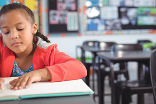 photo - Girl Writing While Sitting at Desk in Classroom