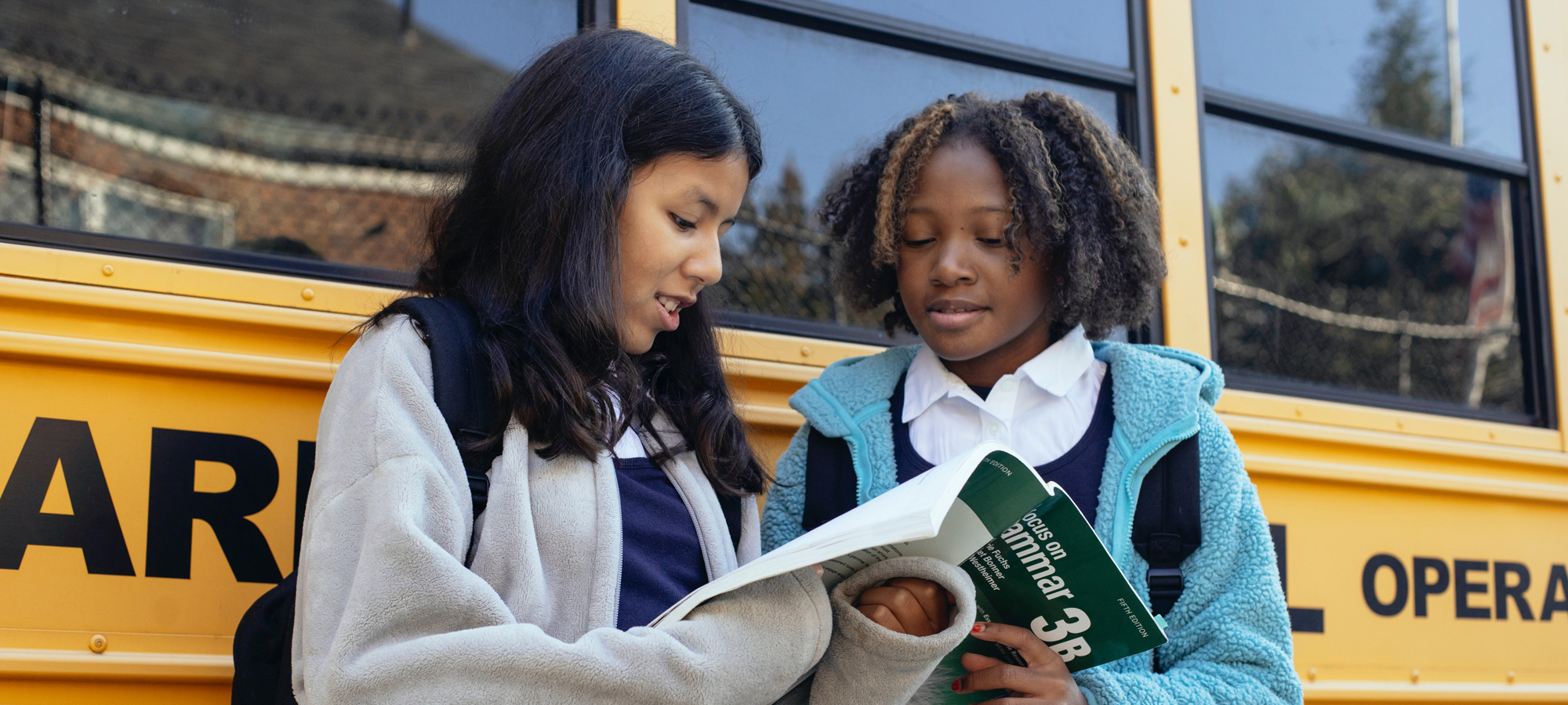 photo - Two students reading by their school bus