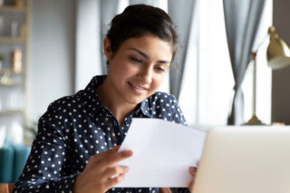 photo - High School Student Reading Paper in Front of Laptop at Home