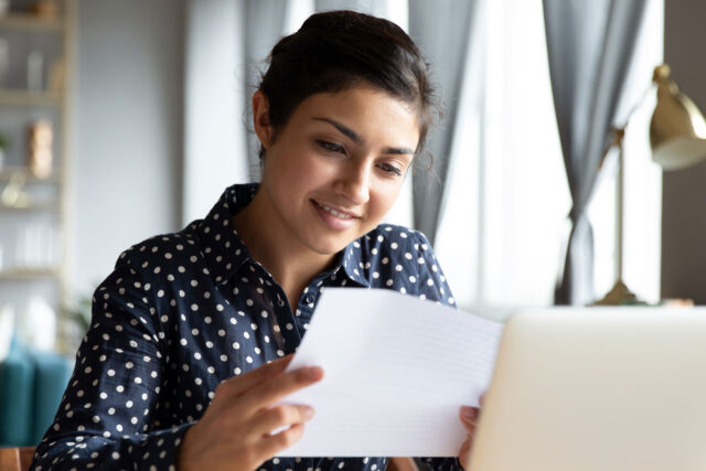 photo - High School Student Reading Paper in Front of Laptop at Home