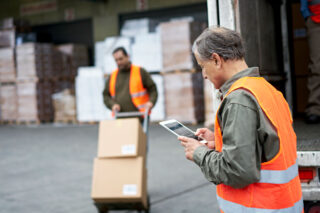 photo - Transport Workers Moving Boxes with Hand Truck and Checking Shipping Order on Tablet