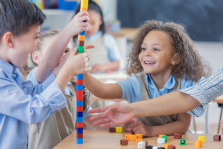 photo - Young Students in Uniform Using Counting Cubes in Classroom with Teacher