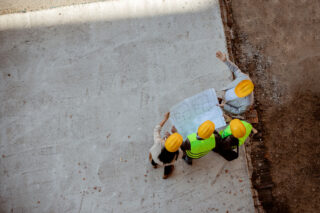 photo - Top View of Architects and Engineer Workers with Blueprints Discussing at Construction Site
