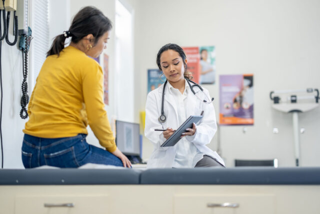photo - Woman Sitting on Exam Table While Doctor Shows Her Information