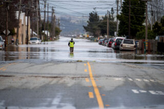 photo - A Person Walks through Floodwaters Downstream from a Levee Breach, pixel-ca-dwr-2023_03_12_KJ_0860_Pajaro_Levee_Break