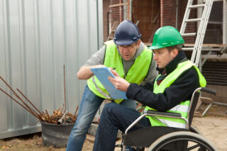 photo - Man in Wheelchair and Hard Hat Working on Paperwork at Construction Site