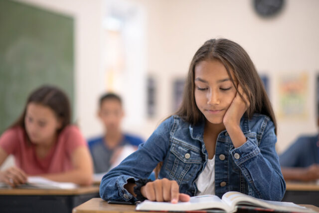 photo - Student Reading Text Book at Desk in Classroom