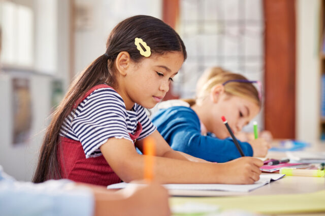 photo - Elementary school student writing at desk in classroom