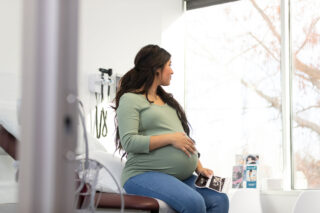 photo - Pregnant Woman Holding Ultrasound and Sitting on Exam Table