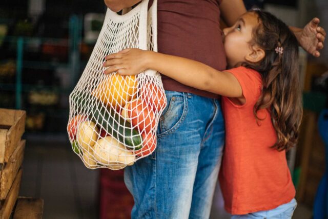 photo - Daughter Hugs Mother Who Is Holding Bag Full of Vegetables