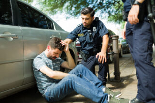 photo - Distressed Man Sitting Against Car on Sidewalk with Two Police Officers
