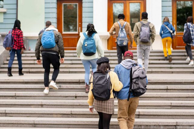 photo - Rear View of Students Carrying Backpacks and Climbing up Steps towards the University Entrance