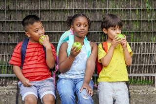 photo - Three Children Wearing Backpacks and Eating Apples