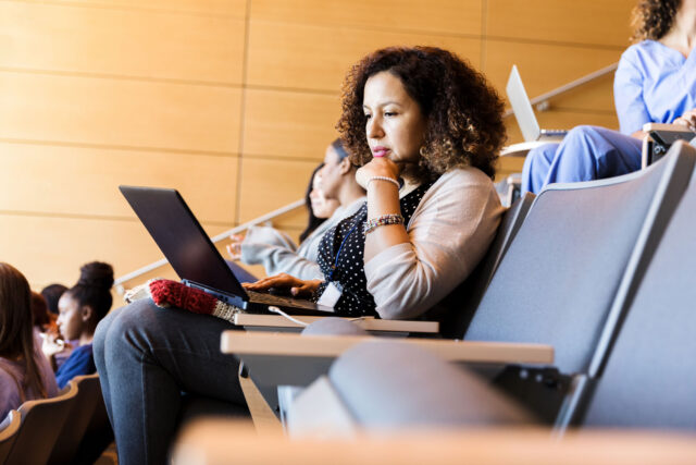 photo - College Student Working on Laptop in Lecture Hall