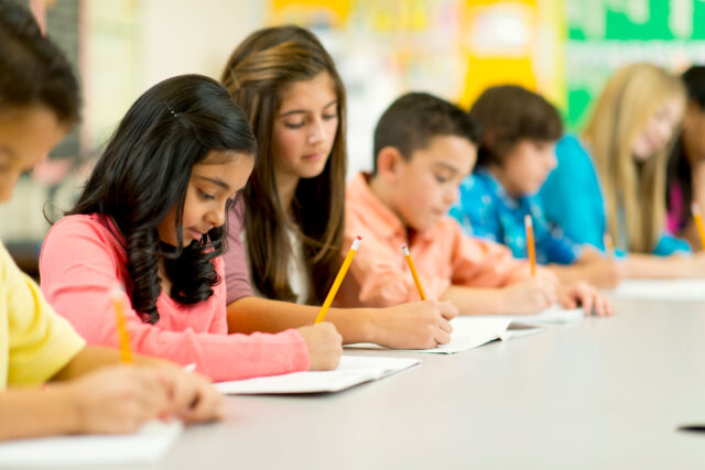 photo - Students Writing with Pencils in a Row in Classroom