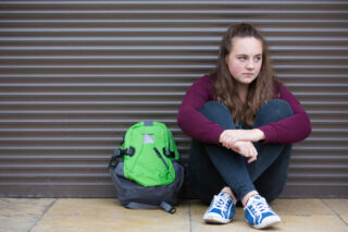 photo - Sad Teenage Girl with Backpack Sitting on Street