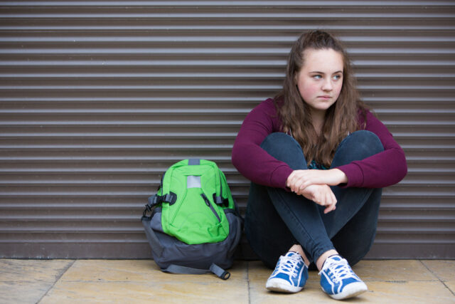 photo - Sad Teenage Girl with Backpack Sitting on Street