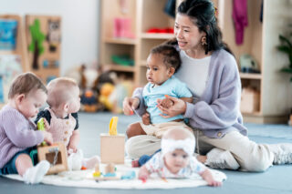 photo - Child Care Worker Interacts with a Group of Babies in a Playful Daycare Environment