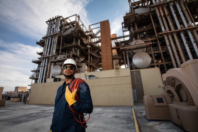 photo - Worker Wearing Hard Hat and Safety Gloves in Front of a Gas Powered Power Station