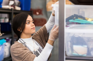 photo - Young Worker Wears Protective Gloves as She Retrieves Cleaning Supplies from the Supple Closet