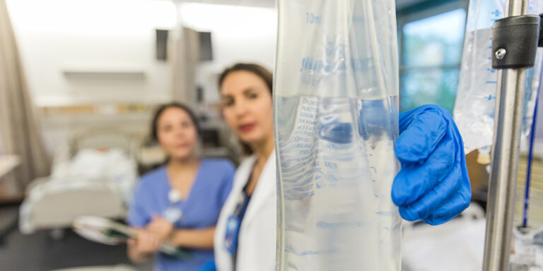 photo - Close Up Photo of IV Fluid Bag with Medical Personnel in the Background