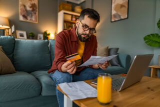 photo - Man Sitting on Couch and Seriously Looking at Bill while Holding Credit Card