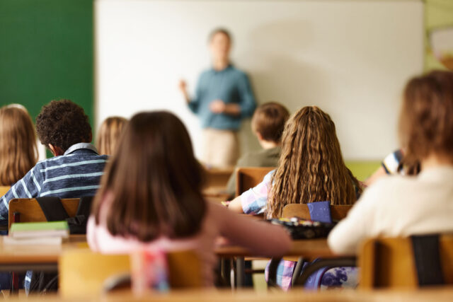 photo - Rear View of Students in Classroom and Teacher Standing in Front of the Class