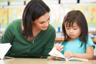 photo - A Teacher and Young Student Looking a Book Together in Elementary School Classroom