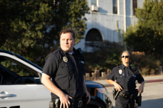 photo - Policeman and Policewoman Looking Off Camera Near Police Car