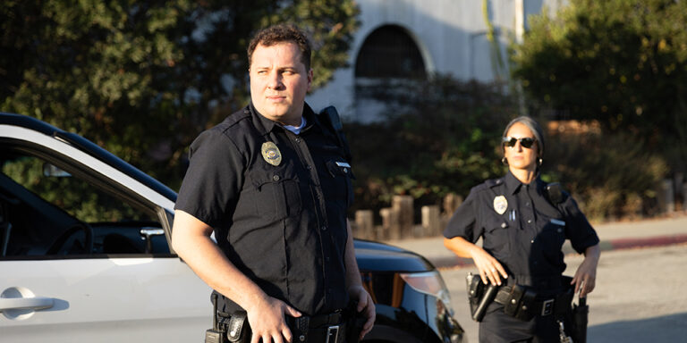 photo - Policeman and Policewoman Looking Off Camera Near Police Car
