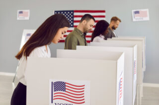 photo - Four Voters at Polling Booths with US Flag Behind Them