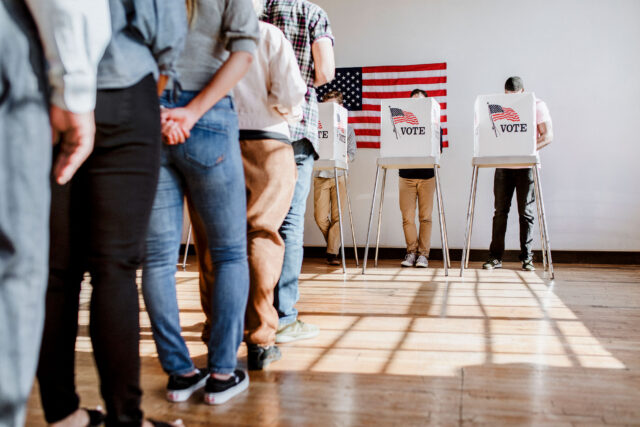 photo - People Waiting in Line and Voting in Booths at Polling Place