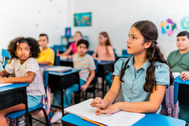 photo - A Student Looking Up at Teacher and Sitting at a Desk in Classroom