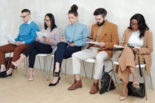 photo - People Waiting and Sitting in Line on Chairs against a Wall