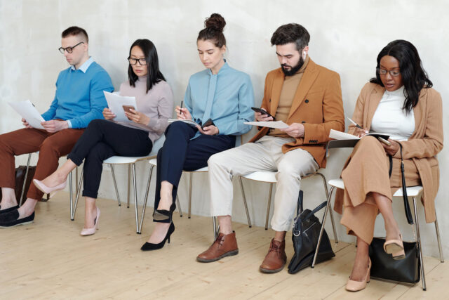 photo - People Waiting and Sitting in Line on Chairs against a Wall