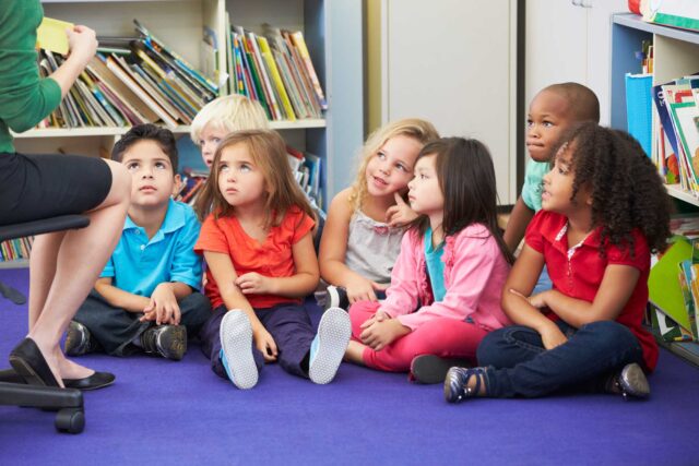photo - Kindergarteners in Classroom Sitting on Rug and Listening to Their Teacher