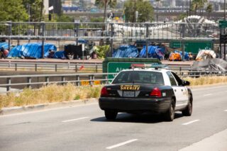 photo - Los Angeles County Sheriff Car Driving Next to Freeway and Homeless Tents