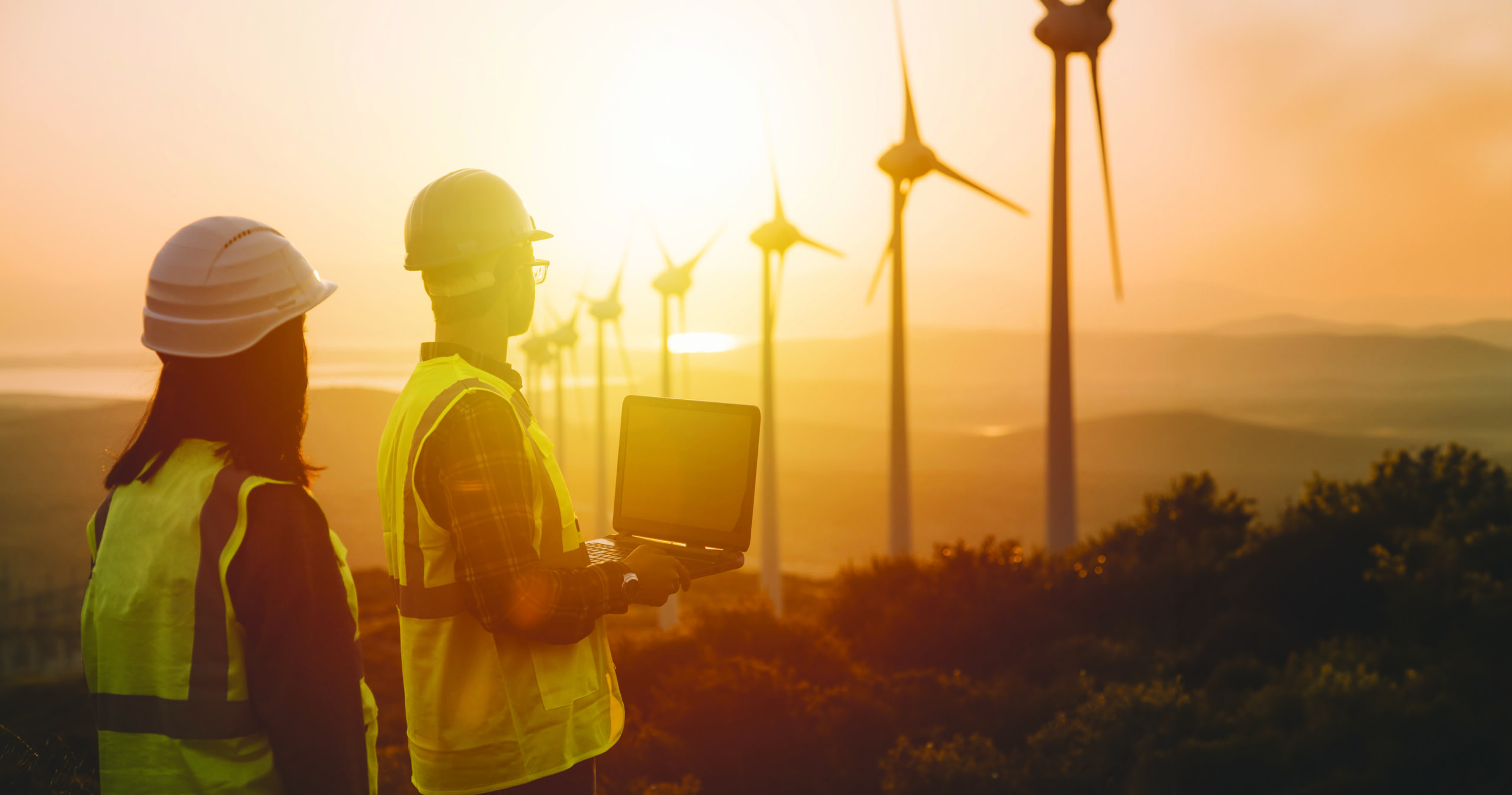 Young maintenance engineer team working in wind turbine farm at sunset