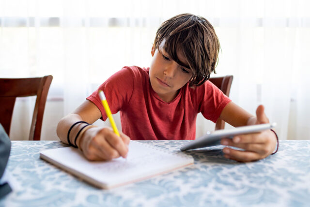 photo - Boy Doing Schol Work from Home with Pen, Paper, and Tablet
