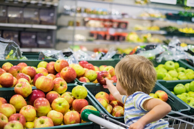 photo - Boy Sitting in Grocery Store Cart Reaching for Apple from Produce Display